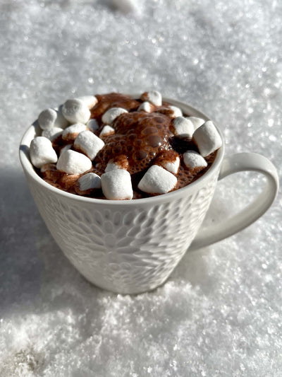 Hot chocolate with mini marshmellows in a large decorative mug sitting in snow 