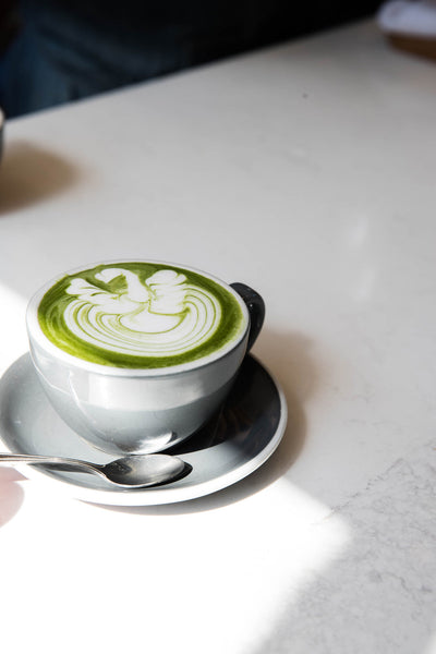 A matcha tea with a foamed milk poured to create a swan on the top all in a capuccino sized cup with saucer 
