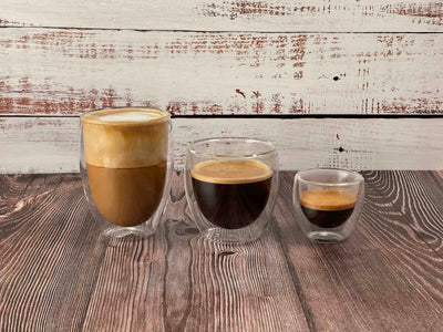 Three different sized double wall glass from Central bru in line from largest to smallest, left to right.  Largest contains a latte, medium contains and Americano and smallest contains and espresso shot.